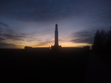 a photo of a monument tower with a wall surrounding it visble with the sunset in the background